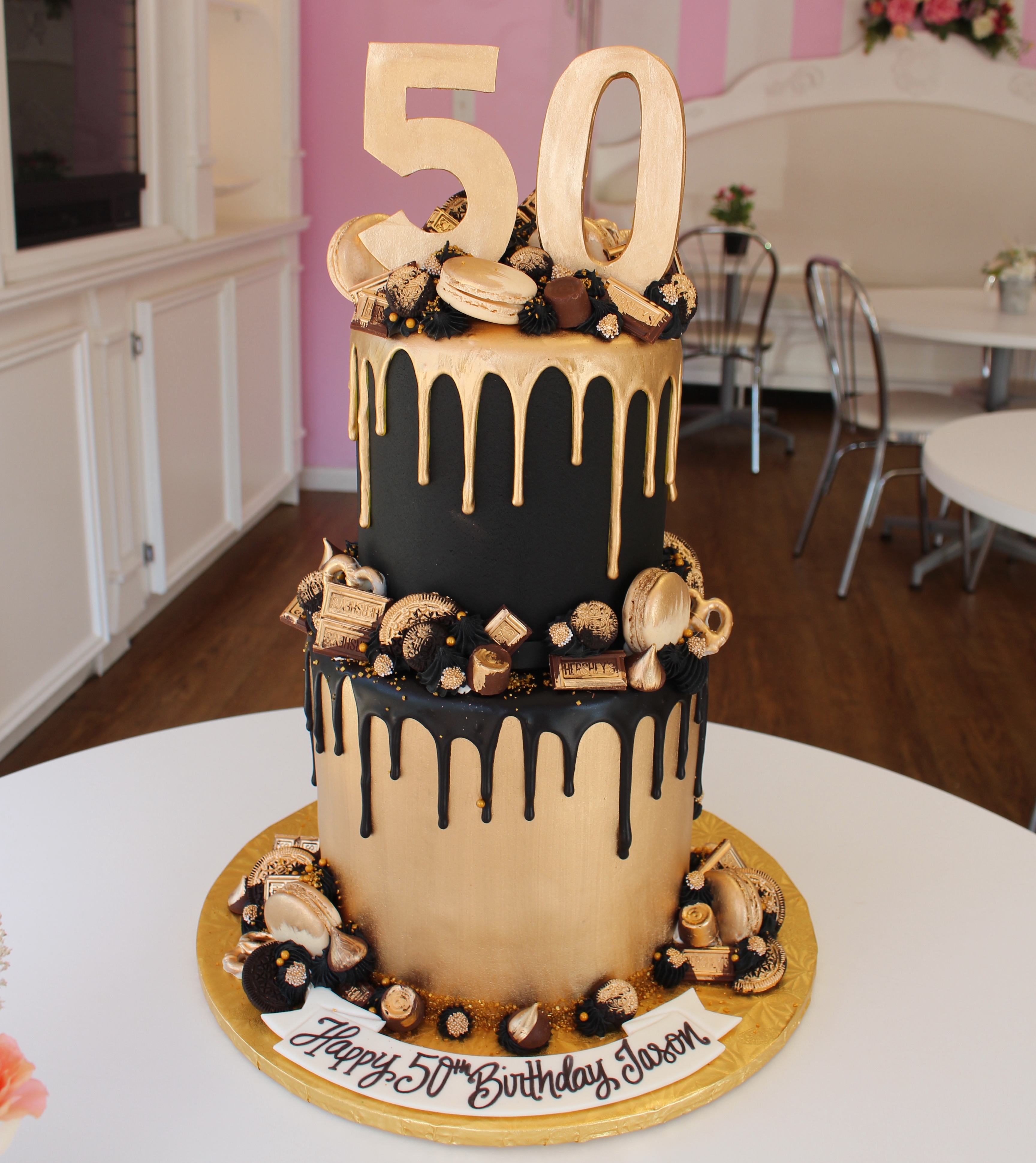Two Tier Black and Gold Drip Cake with Gold Brushed Macarons, Cookies, and Candies